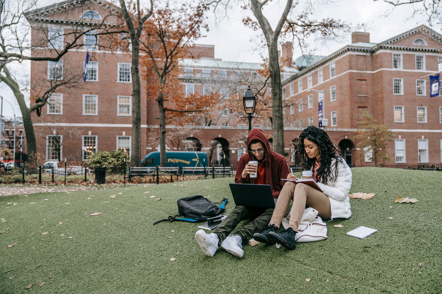 photographic | two students sitting together on campus grass talking comfortably with books open