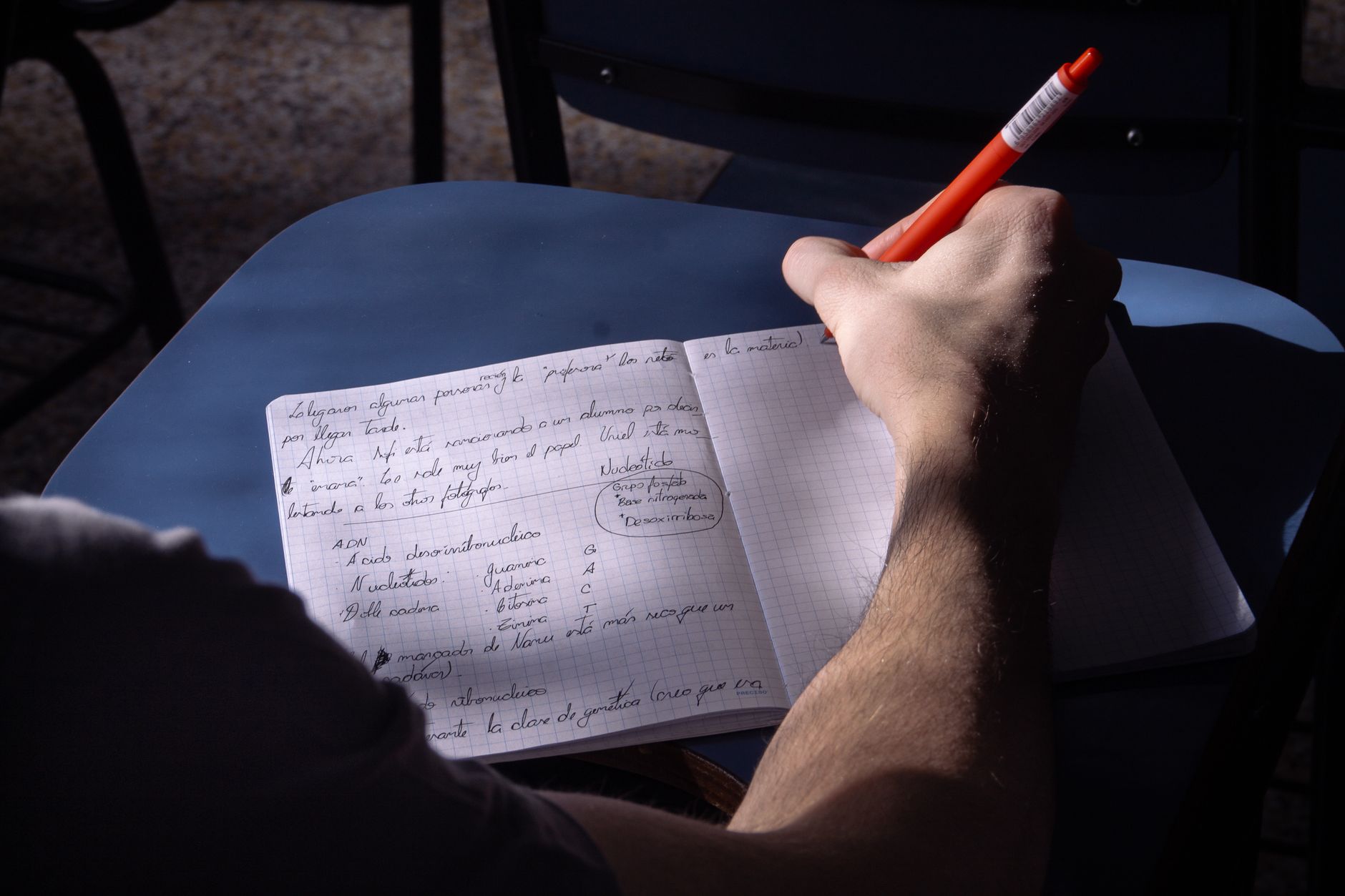 photographic | a high school student sitting at a wooden desk writing notes in a notebook with history textbooks open